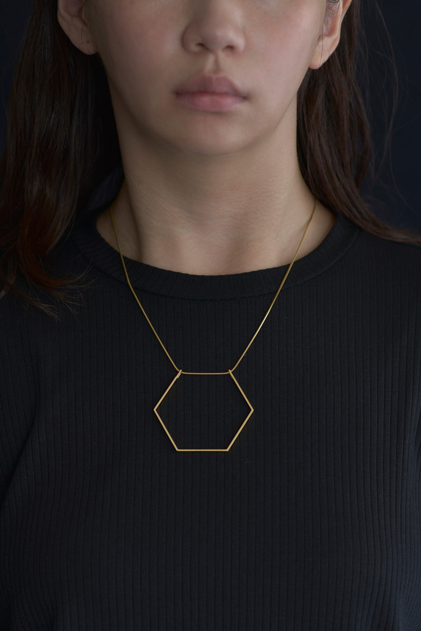 6角形(Hexagon)の形をしたシンプルな、真鍮製アクセサリーのネックレスをつけた女性モデル