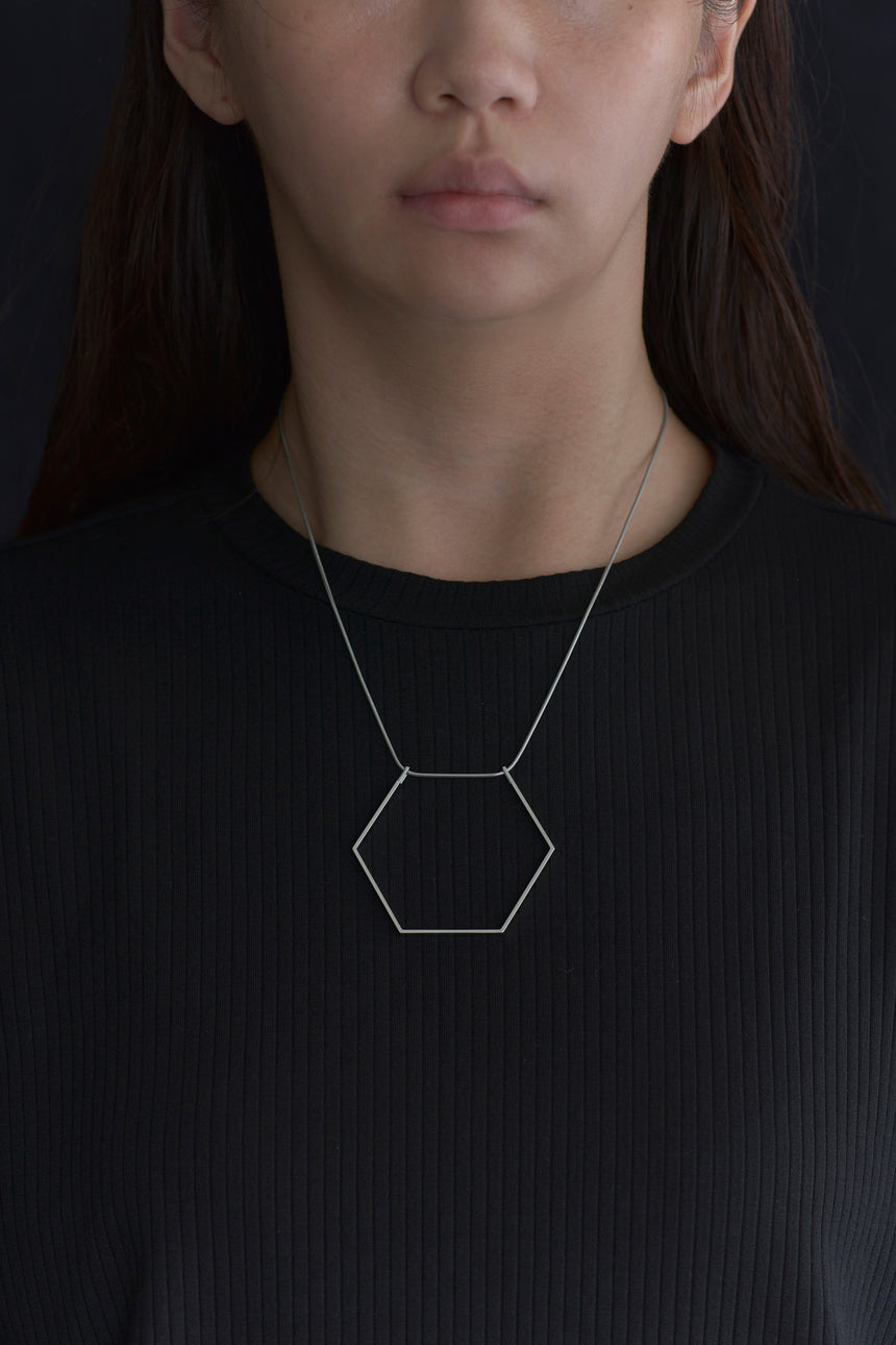 6角形(Hexagon)の形をしたシンプルな、真鍮製アクセサリーのネックレスをつけた女性モデル