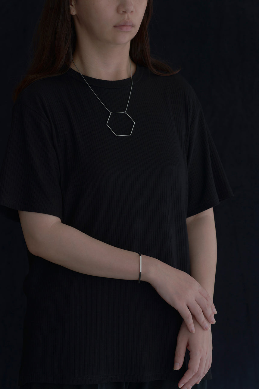 6角形(Hexagon)の形をしたシンプルな、真鍮製アクセサリーのネックレスとバングルをつけた女性モデル