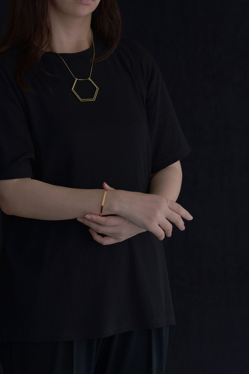 6角形(Hexagon)の形をしたシンプルな、真鍮製アクセサリーのネックレスとバングルをつけた女性モデル