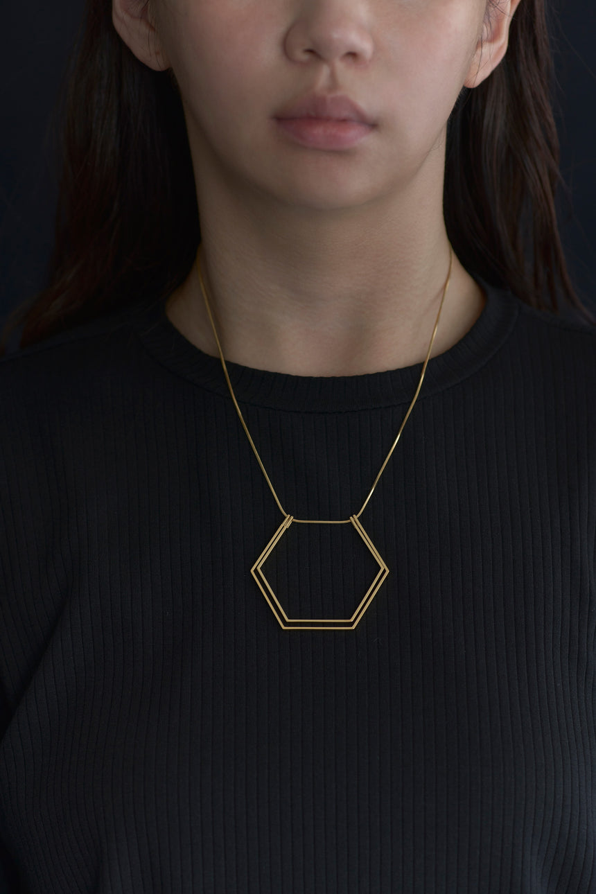 6角形(Hexagon)の形をしたシンプルな、真鍮製アクセサリーのネックレスをつけた女性モデル