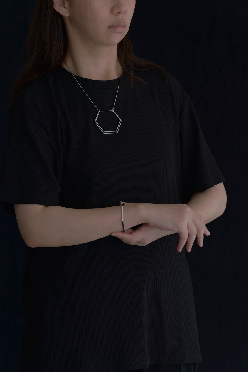 6角形(Hexagon)の形をしたシンプルな、真鍮製アクセサリーのネックレスとバングルをつけた女性モデル