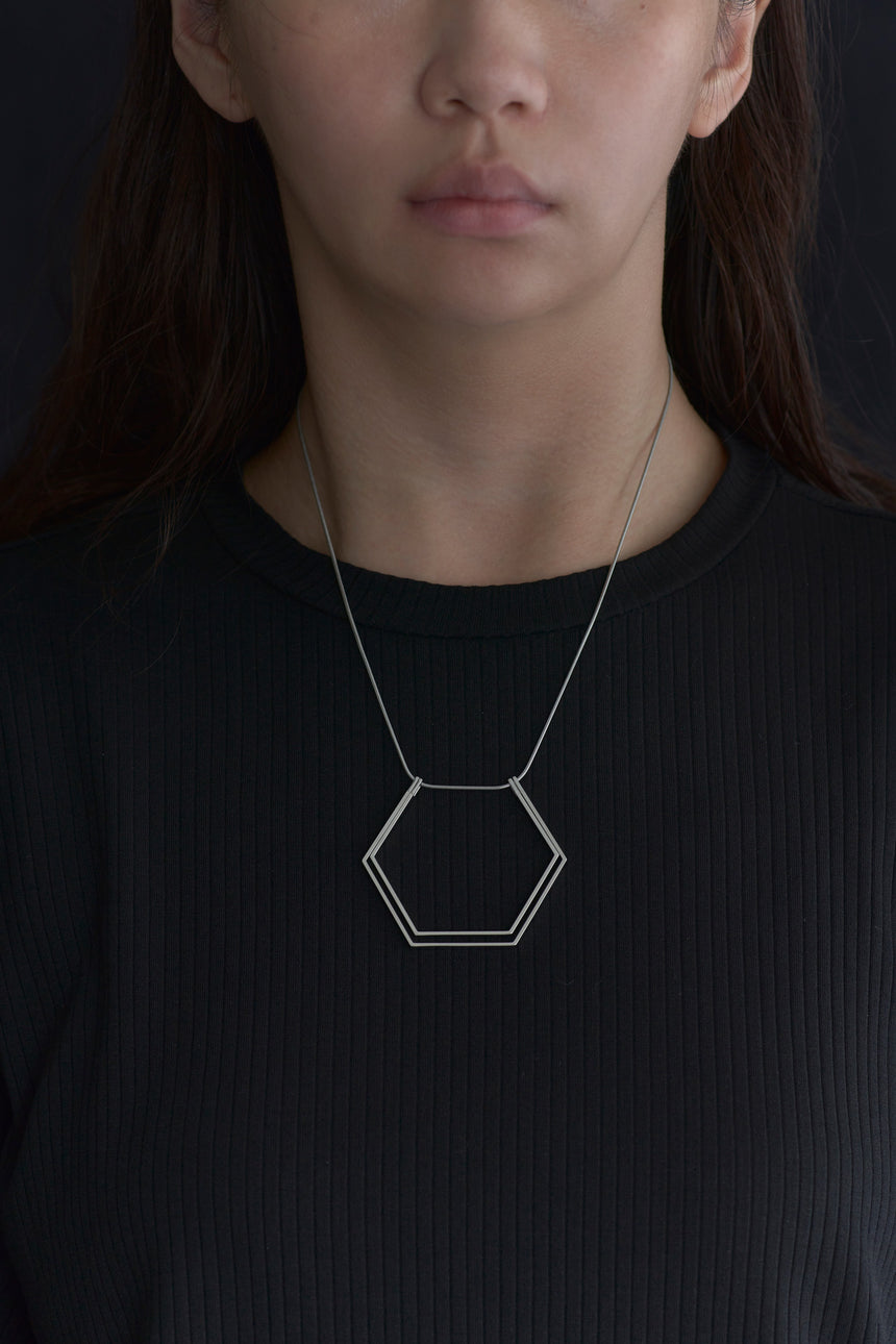 6角形(Hexagon)の形をしたシンプルな、真鍮製アクセサリーのネックレスをつけた女性モデル
