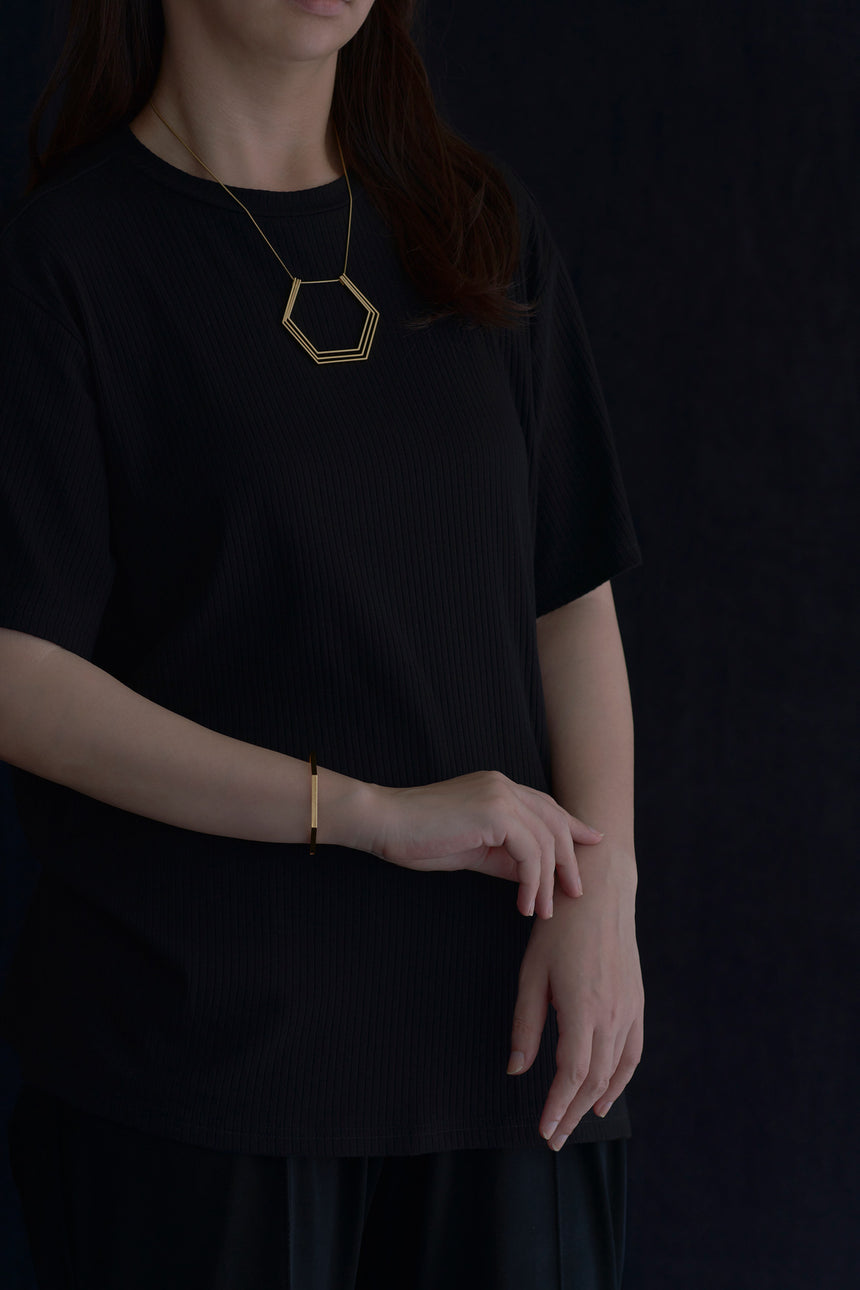 6角形(Hexagon)の形をしたシンプルな、真鍮製アクセサリーのネックレスとバングルをつけた女性モデル