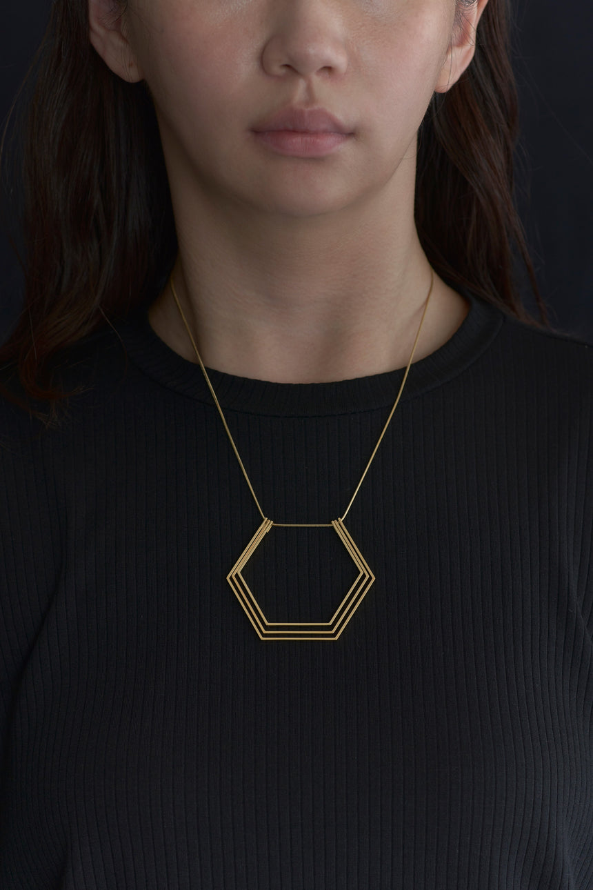 6角形(Hexagon)の形をしたシンプルな、真鍮製アクセサリーのネックレスをつけた女性モデル