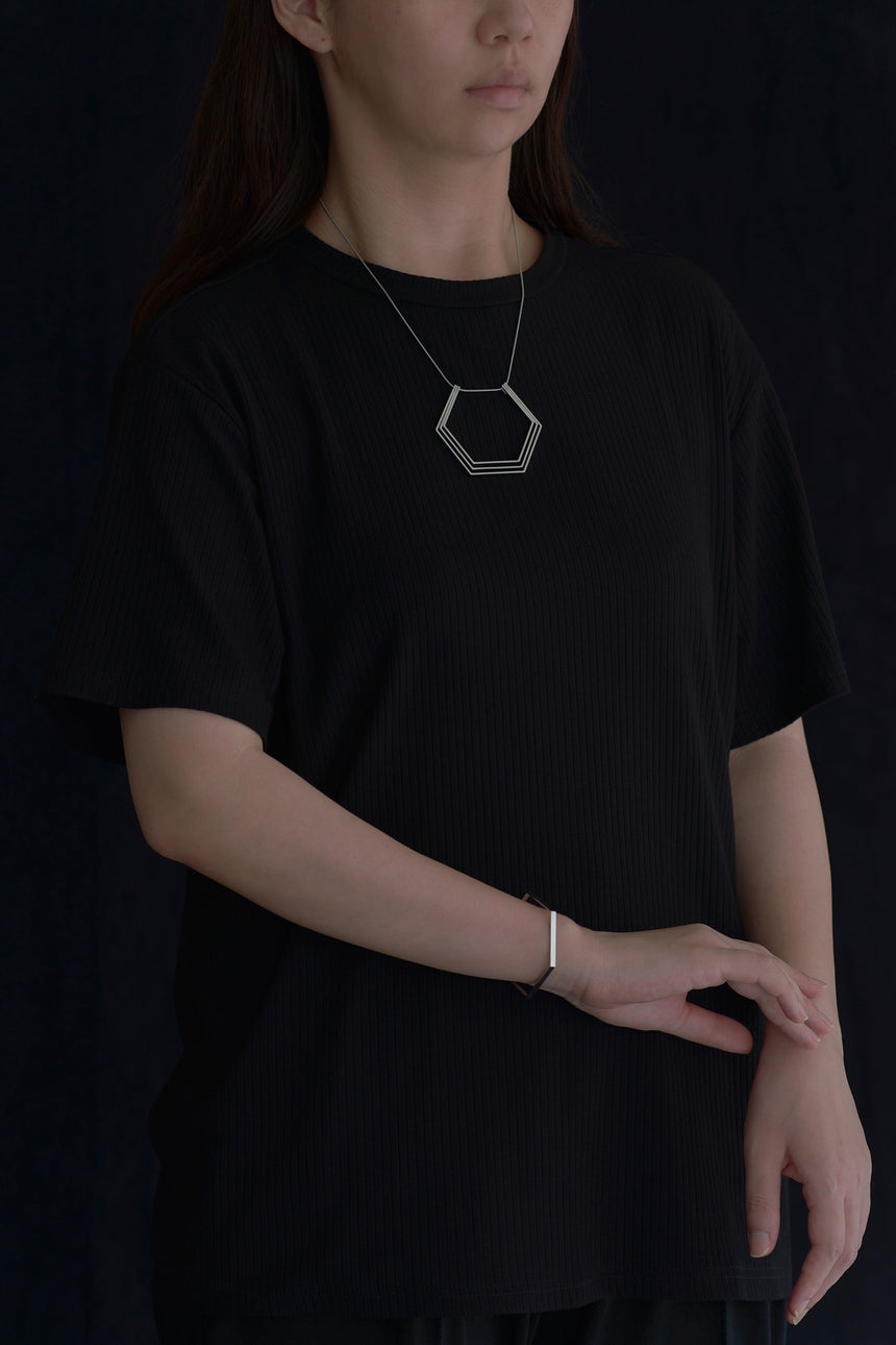 6角形(Hexagon)の形をしたシンプルな、真鍮製アクセサリーのネックレスとバングルをつけた女性モデル