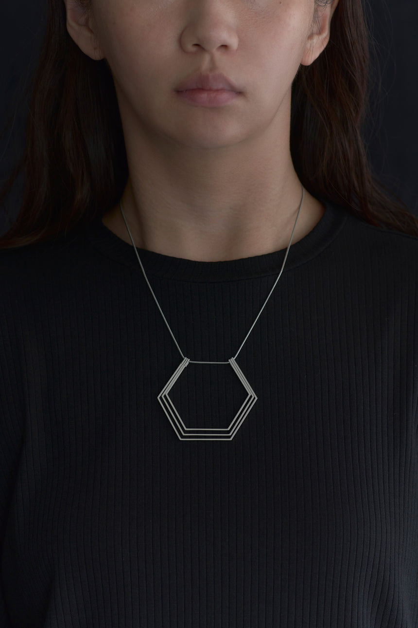 6角形(Hexagon)の形をしたシンプルな、真鍮製アクセサリーのネックレスをつけた女性モデル