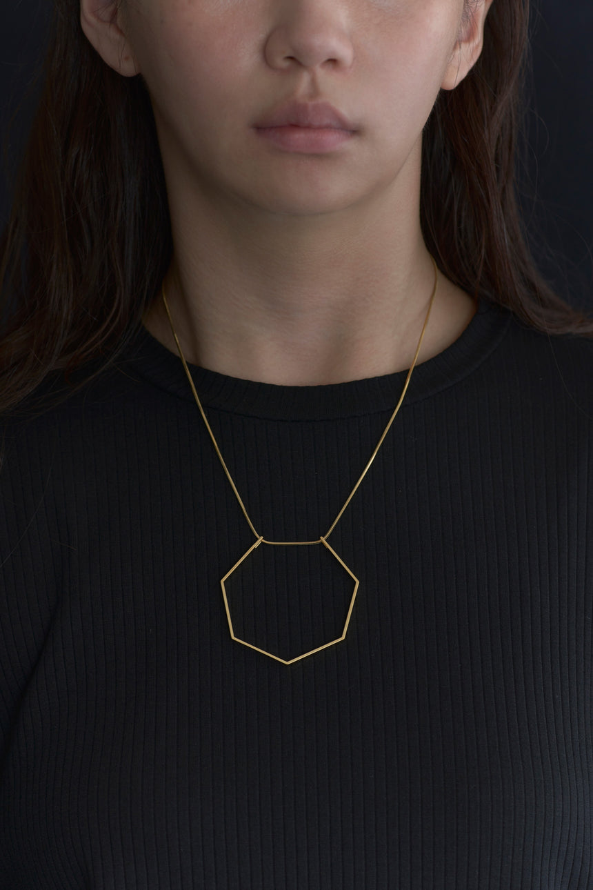 7角形(Heptagon)の形をしたシンプルな、真鍮製アクセサリーのネックレスをした女性モデル