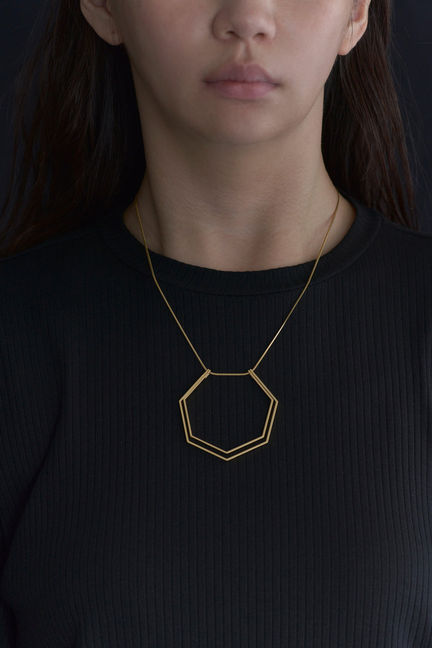 7角形(Heptagon)の形をしたシンプルな、真鍮製アクセサリーのネックレスをつけた女性モデル