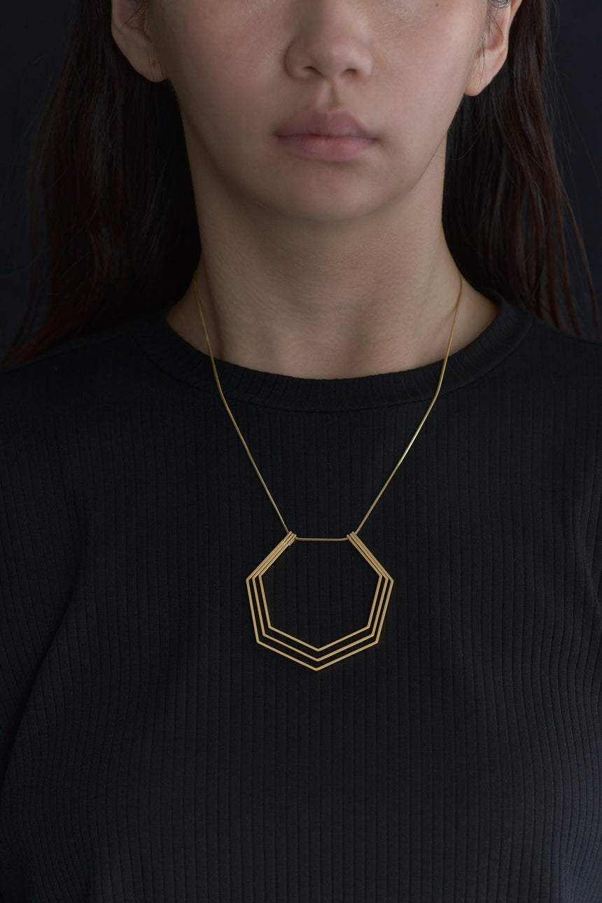 7角形(Heptagon)の形をしたシンプルな、真鍮製アクセサリーのネックレスをつけた女性モデル