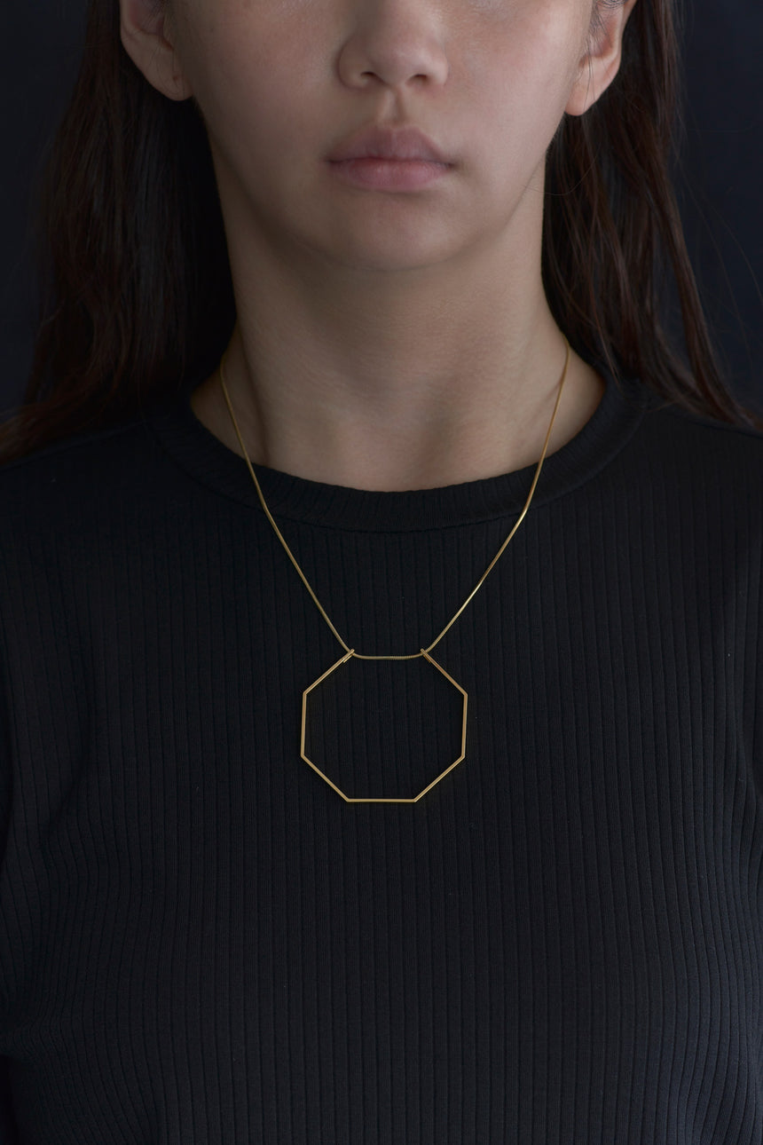 8角形(Octagon)の形をしたシンプルな、真鍮製アクセサリーのネックレスをつけた女性モデル