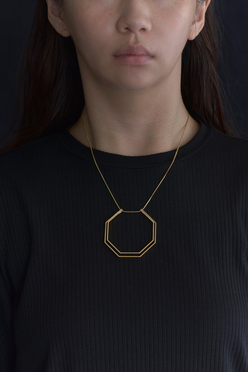 8角形(Octagon)の形をしたシンプルな、真鍮製アクセサリーのネックレスをした女性モデル