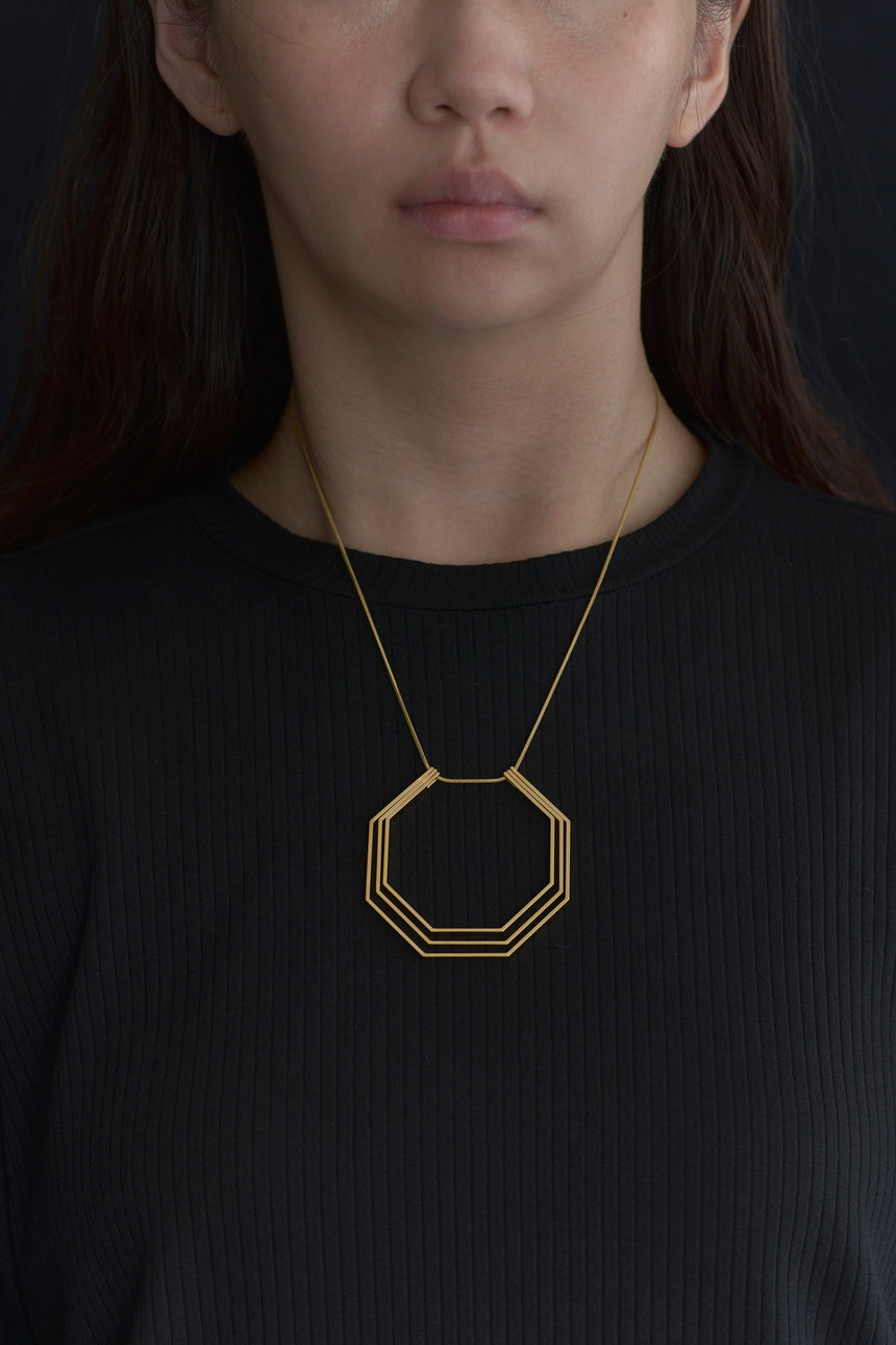 8角形（Octagon）の形をしたシンプルな、真鍮製アクセサリーのネックレスをした女性モデル