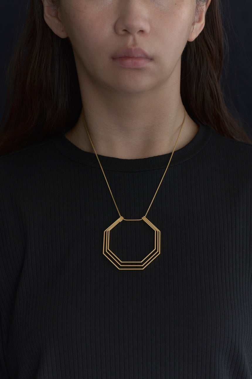 8角形(Octagon)の形をしたシンプルな、真鍮製アクセサリーのネックレスをした女性モデル