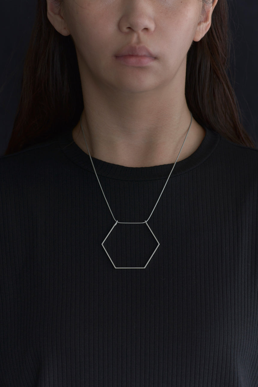6角形（Hexagon）の形をしたシンプルな、真鍮製アクセサリーのネックレスをつけた女性モデル