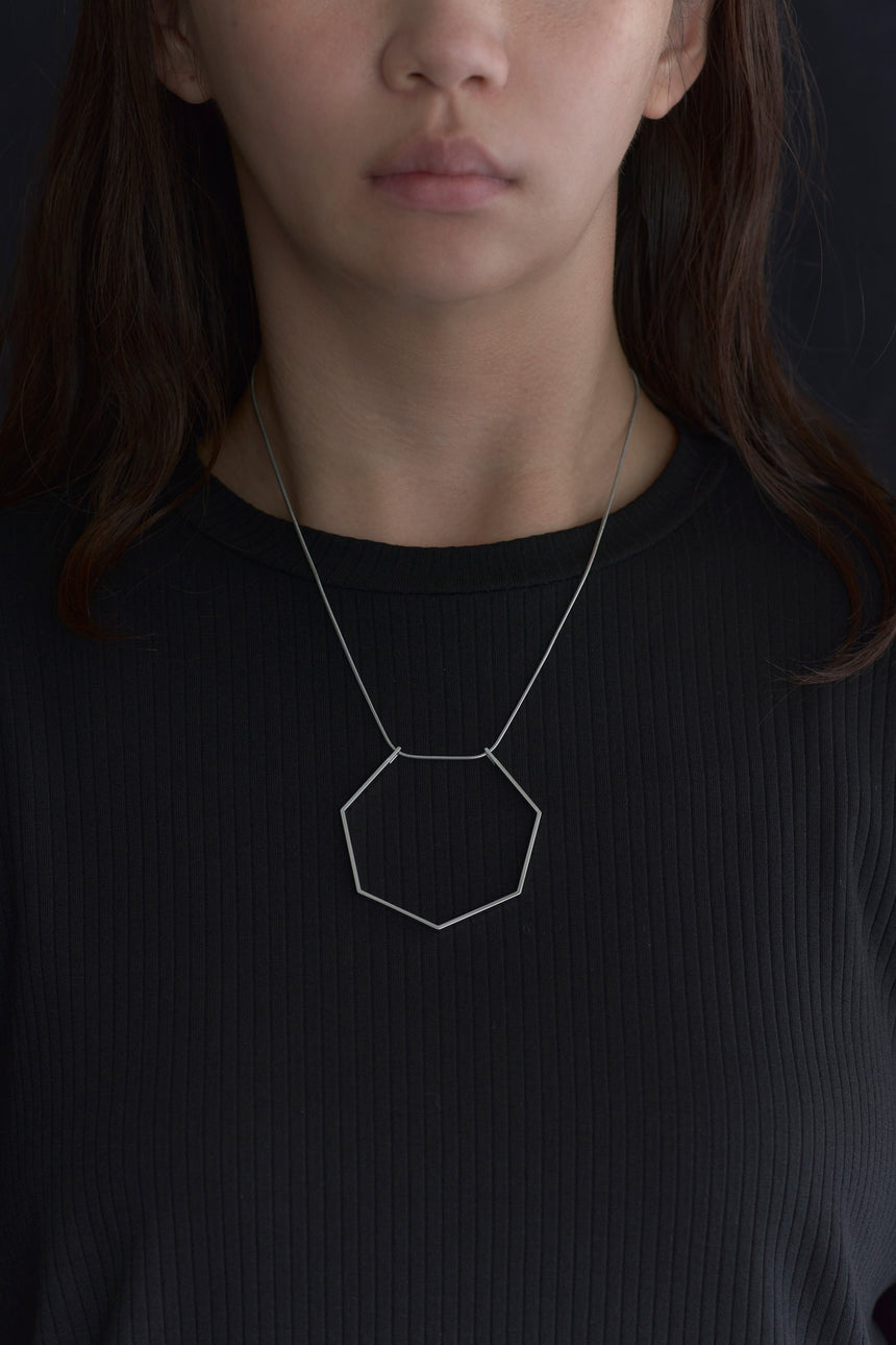 7角形の形をしたシンプルな、真鍮製アクセサリーのネックレスをつけた女性モデル