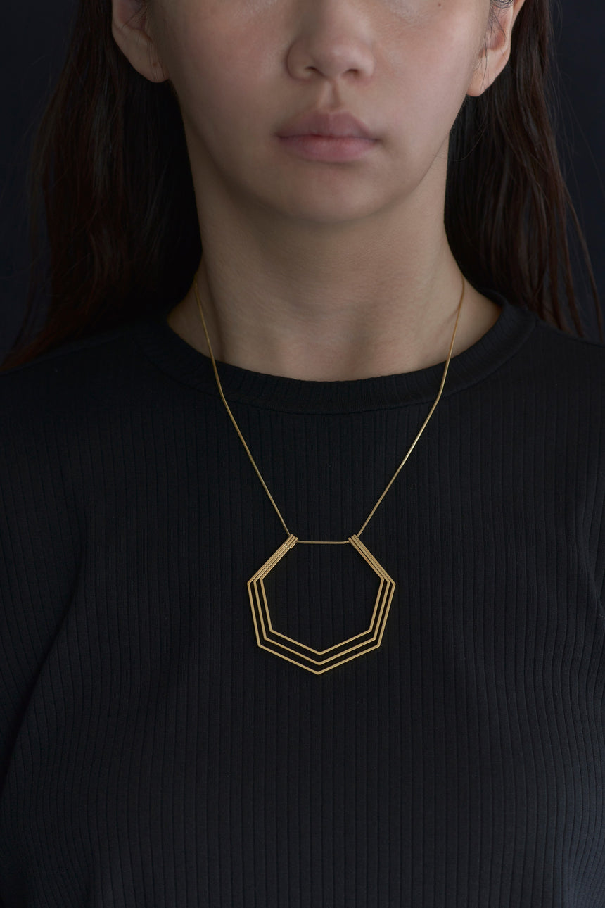 7角形（Heptagon）の形をしたシンプルな、真鍮製アクセサリーのネックレスをつけた女性モデル