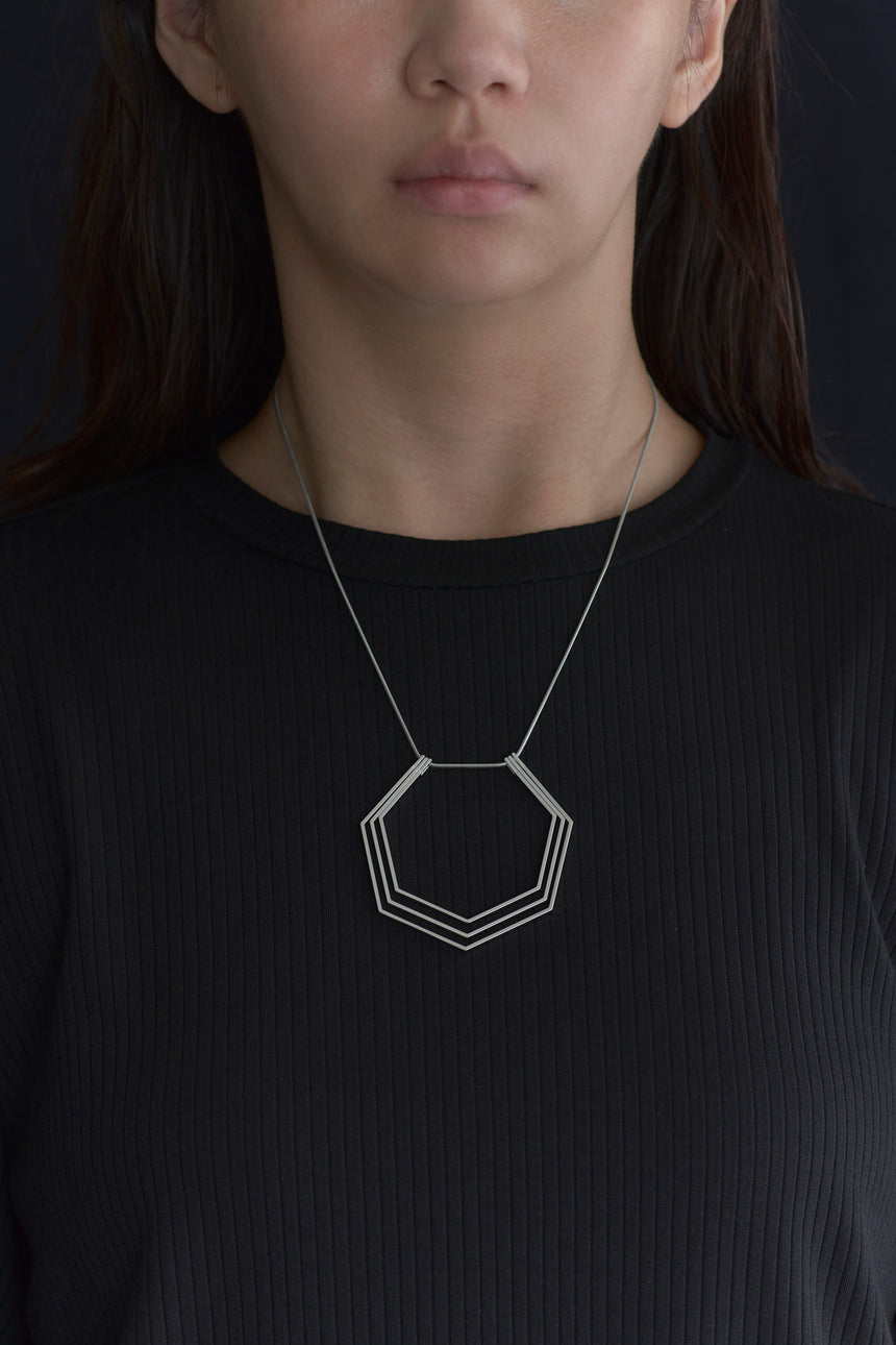 7角形の形をしたシンプルな、真鍮製アクセサリーのネックレスをつけた女性モデル