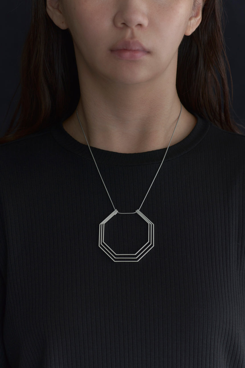 8角形の形をしたシンプルな、真鍮製アクセサリーのネックレスをつけた女性モデル
